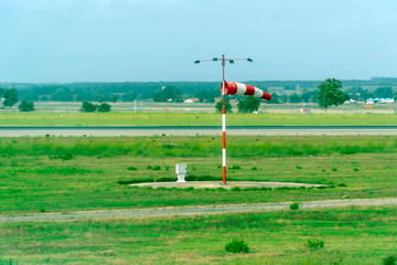 A red white windsock on a windy day at a green airport runway measuring the wind speed as an...