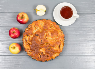 Homemade baked apple pie, in a plate, on a gray wooden table, ready to eat. View from above.