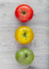 Three different colour tomatoes like a semaphore placed on the gray qooden table. Flat lay view....