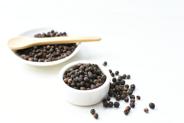 Black peppercorns in bowls on white wooden background