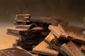 Bars of dark chocolate sprinkled with cocoa powder in light smoke. Close up, chocolate day concept
