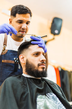 Young Latin Barber At Work In Stylish Barbershop. Cool, bearded man enjoys the moment.
