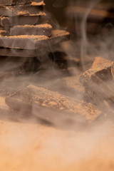 Pieces of dark chocolate bars are visible through thick smoke. Chocolate day concept. Vertical format