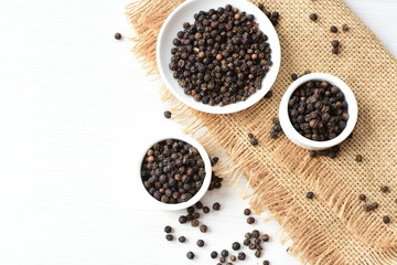 Black peppercorns in bowls on white wooden background