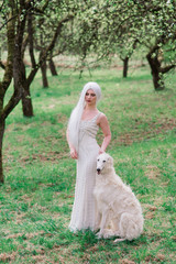 Blonde woman in white dress playing with her russian wolfhound dog in garden.