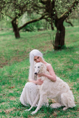 Blonde woman in white dress playing with her russian wolfhound dog in garden.