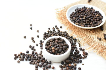 Black peppercorns in bowls on white wooden background
