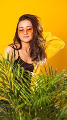 a girl of Asian appearance in yellow glasses, yellow clothes, on a yellow background, looking at the camera, in the foreground there is a large flower