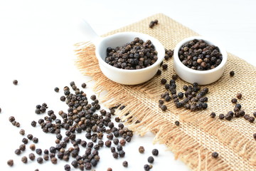 Black peppercorns in bowls on white wooden background
