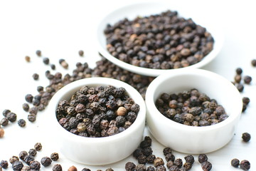 Black peppercorns in bowls on white wooden background