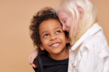 close friendship between two children of different nationalities, beautiful caucasian albino girl and african boy with curly hair, they are hugging - obrazy, fototapety, plakaty
