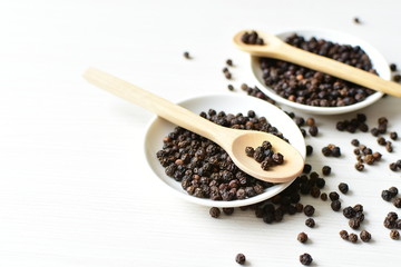 Black peppercorns in bowls on white wooden background