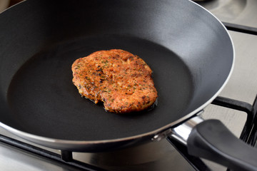 Chicken fillet fried in a pan. Chop is prepared with herbs and spices. Fresh hot roasted meat. Pan is on gas plate. Closeup black background.