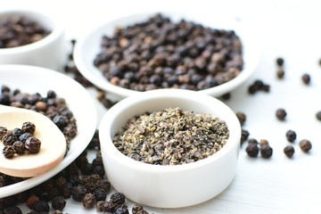 Black peppercorns in bowls on white wooden background