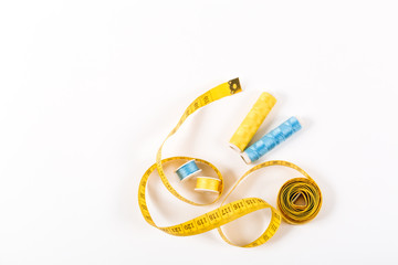 A centimeter tape and two spools of yellow and blue thread on a white background in a minimalistic style with a place for text. Items for needlework, embroidery, sewing and cutting clothes.