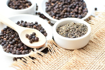 Black peppercorns in bowls on white wooden background