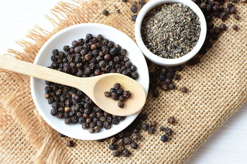 Black peppercorns in bowls on white wooden background