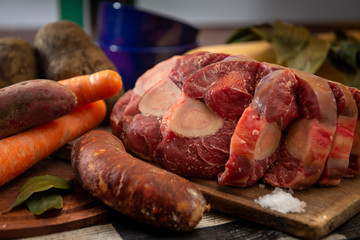 Osobuco carne cruda y chorizo mas ingredientes para preparar un puchero o guiso sobre tabla de madera 