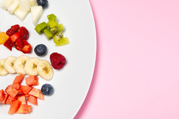Fresh fruit salad on white plate. Mixed fruit in white plate healthy food style. Useful fruit salad of fresh fruits and berries on pink background