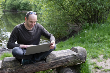 Fototapeta premium a man sits on a log and works with a laptop near the lake