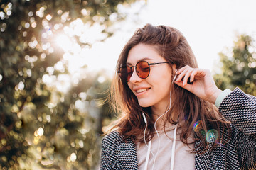 beautiful young woman with a smile listens to music from the phone in headphones in the park