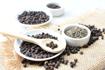 Black peppercorns in bowls on white wooden background