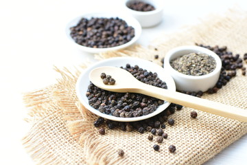 Black peppercorns in bowls on white wooden background