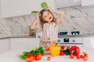 Little girl cooking salad and makes ears of lettuce in kitchen at home.