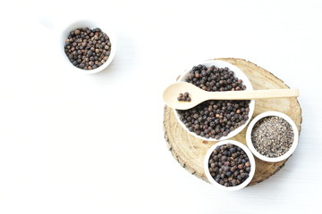 Black peppercorns in bowls on white wooden background
