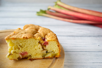 A piece of sponge cake with rhubarb on a white wooden background