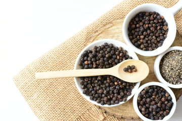 Black peppercorns in bowls on white wooden background