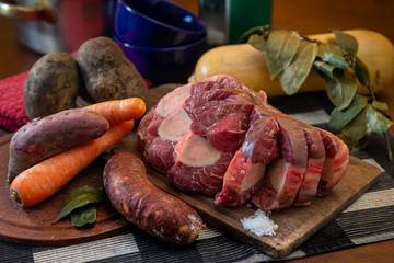 Osobuco carne cruda y chorizo mas ingredientes para preparar un puchero o guiso sobre tabla de madera 