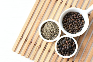 Black peppercorns in bowls on white wooden background