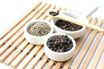 Black peppercorns in bowls on white wooden background