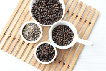 Black peppercorns in bowls on white wooden background