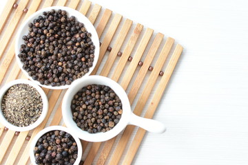 Black peppercorns in bowls on white wooden background