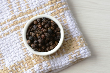 Black peppercorns in bowls on white wooden background