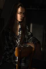 the girl sits on a chair in a plaid shirt, put her hands on the back of the chair, the ray of the...