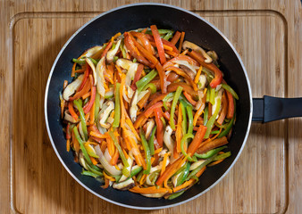 Black frying pan with different colored vegetables and shiitake mushrooms on a wooden table.