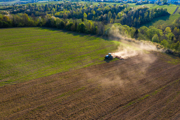 Farmer cultivates a field on a crawler tractor and loosens the soil with a disc cultivator against the backdrop of forest and blue sky.