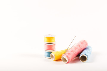 Three spools and bobbins of thread of yellow, blue and pink color with needles on a white background in a minimalistic style with a place for text. Items for needlework, embroidery and sewing.