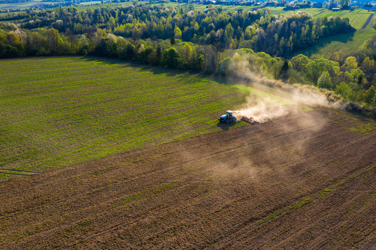 Farmer Cultivates A Field On A Crawler Tractor And Loosens The Soil With A Disc Cultivator Against The Backdrop Of Forest And Blue Sky.