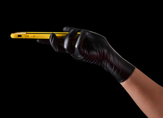 Hand in black glove holding mobile phone with blank screen isolated on black