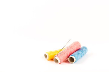 Three spools and bobbins of thread of yellow, blue and pink color with needles on a white background in a minimalistic style with a place for text. Items for needlework, embroidery and sewing.