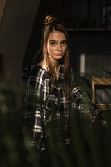 Fototapeta na wymiar the girl sits on a chair in a plaid shirt, put her hands on the back of the chair, the ray of the sonde falls on her face