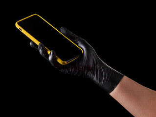 Hand in black glove holding mobile phone with blank screen isolated on black