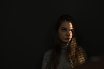 Fototapeta premium portrait of a girl against a dark background, the light from the window falls on the girl’s face, I create shadow stripes on the blinds