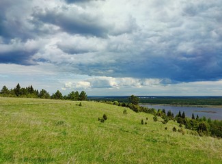 gloomy clouds in the blue sky over the mountain with green grass and trees near the river