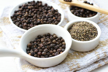 Whole and ground black peppercorns on white wooden background
