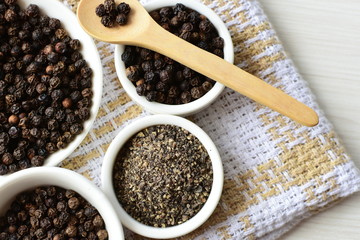 Whole and ground black peppercorns on white wooden background